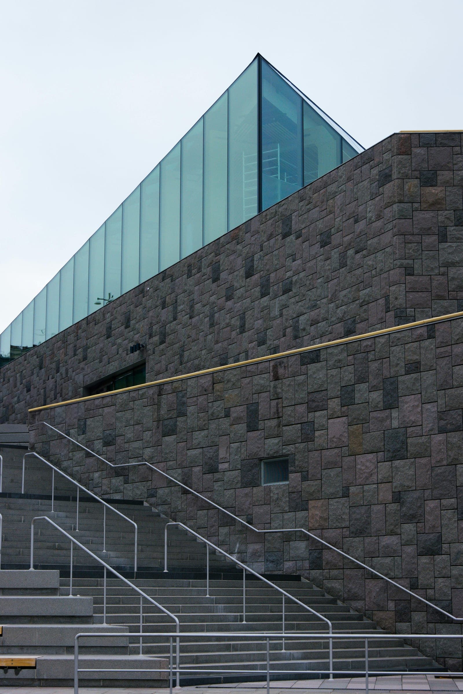 Low-angle view of a modern glass facade reflecting blue sky and clouds, diagonal edge against open sky.